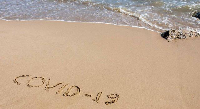 ¿Cómo afectan los ERTE a las vacaciones? Imagen de playa con las palabras covid-19 escrito en la arena