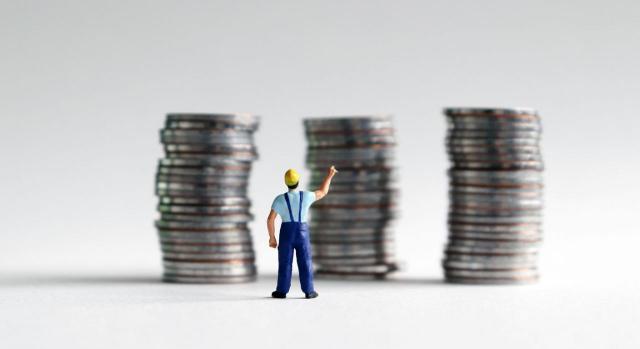 Acuerdo para incrementar el SMI en 2021. Imagen de hombre en miniatura frente a columnas grandes de monedas