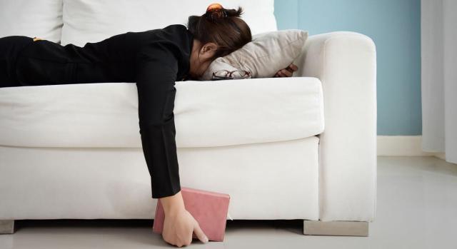 Mujer cansada tumbada en sofá con una libreta en la mano. Absentismo laboral, integridad física y libertad de empresa