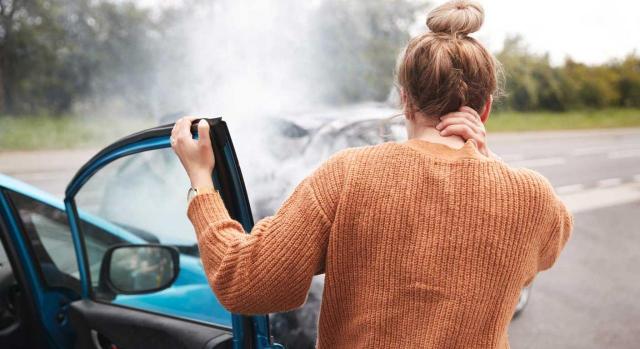 Es accidente in itinere el sufrido por una trabajadora tras abandonar las instalaciones de la empresa para acudir a una cita médica. Imagen de una chica que esta de espalda viendo como se ha quedado el coche de delante tras una colisión y tocándose el cuello como dolorida