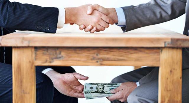 Corrupción en tu organización: cómo denunciarla sin perder tu trabajo Corrupción en tu organización: cómo denunciarla sin perder tu trabajo. Imagen de apretón de manos mientras que por debajo de la mesa, se entregan dinero a escondidas