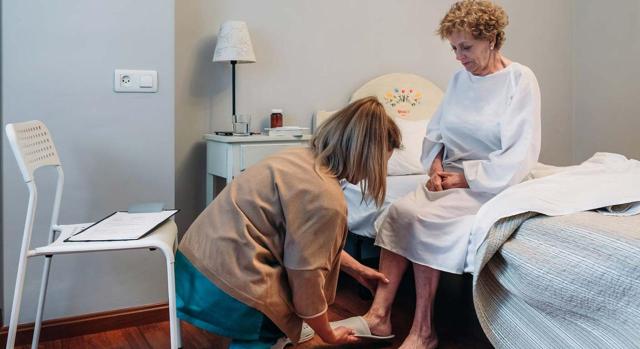La memoria que acompaña al Real Decreto resulta palmariamente insuficiente. Cuidadora a domicilio ayudando a levantarse a una mujer de edad avanzada 