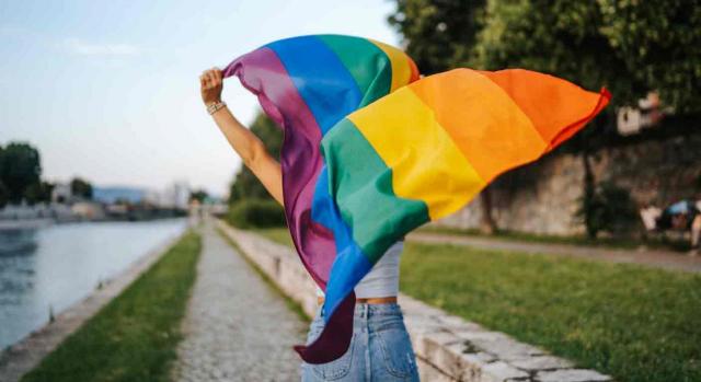 Aprobada Ley trans. Una persona lleva una bandera lgtbi con los brazo en alto
