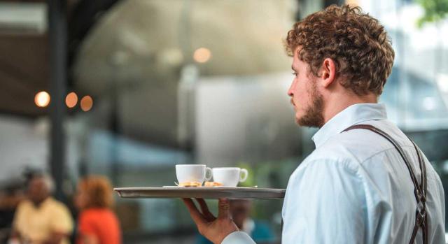 Ausencias injustificadas al puesto de trabajo. ¿La empresa debe despedir o dar de baja por abandono? Imagen de un camarero cuacásico trabajando en una cafetería