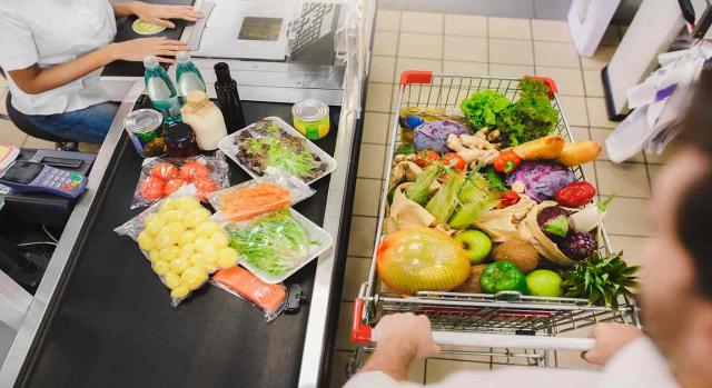 Enfermedad profesional; síndrome del túnel carpiano. Un hombre en la caja de un supermercado con un carro lleno de alimentos y otros en la cinta para pagar