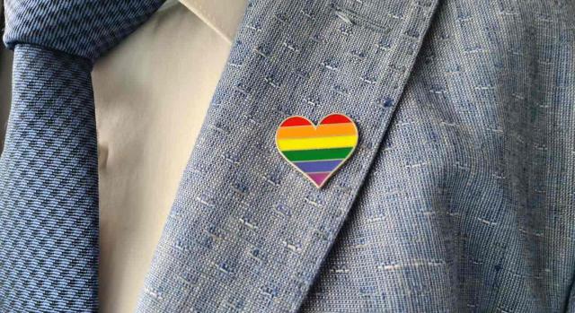 Orientación sexual; trabajador independiente; discriminación. Primer plano de una corbata y chaqueta que lleva en la solapa un pin en forma de corazón y los colores de la bandera LGTB