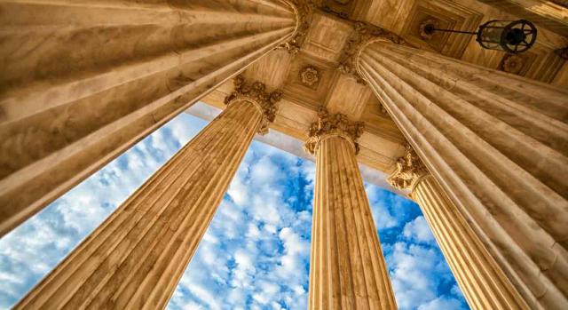 Jurisprudencia. Vista de abajo hacia arriba de unas columnas y el techo de un edificio 