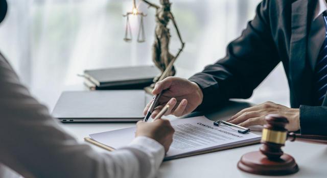 Sentencia de suplicación dictada sin notificar la composición del tribunal y el nombre del ponente. Imagen de unas manos firmando un papel, con martillo y balanza