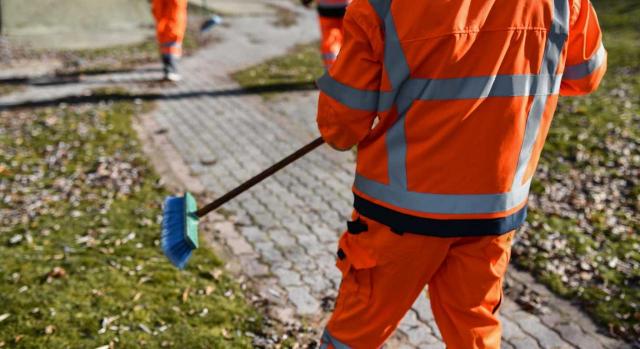 El convenio colectivo de una entidad local debe aplicarse a un trabajador de dicha entidad, aunque su categoría profesional no esté incluida en el convenio. Imagen de unos trabajadores con traje naranja limpiando una acera con un cepillo de limpieza