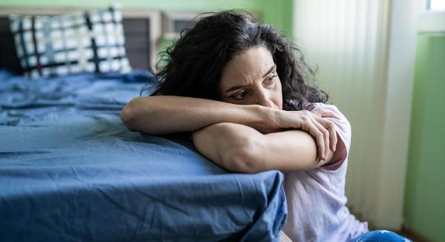 COVID-19; violencia de género; estado de alarma. Imagen de una mujer preocupada sentada al lado de cama