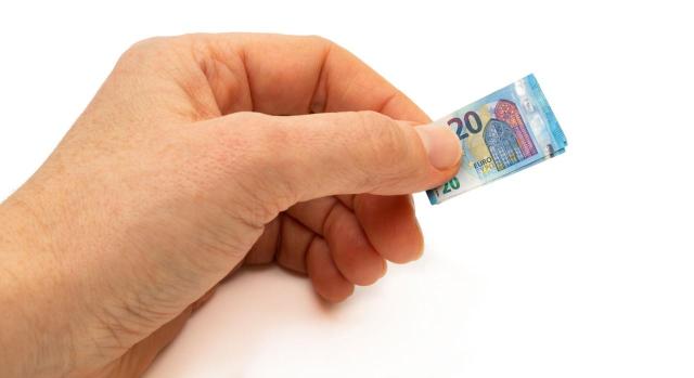 Establecido el importe mínimo no recaudable en prestaciones por desempleo indebidamente percibidas. Imagen de una mano muy grande con un billete de 20 euros muy pequeñito