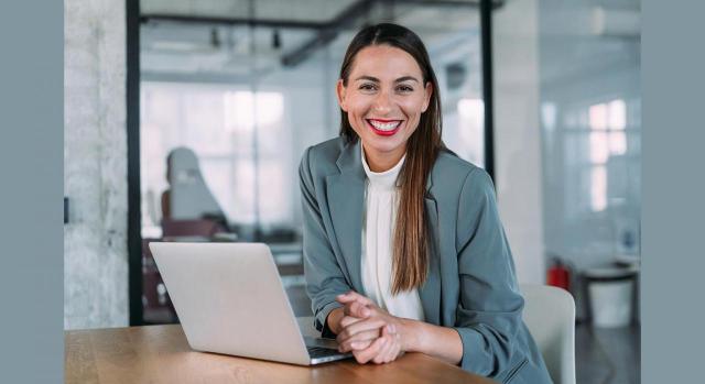 Puntos clave para ejercer como asesor jurídico-laboral. Imagen de mujer sonriente trabajando en la oficina con un portátil