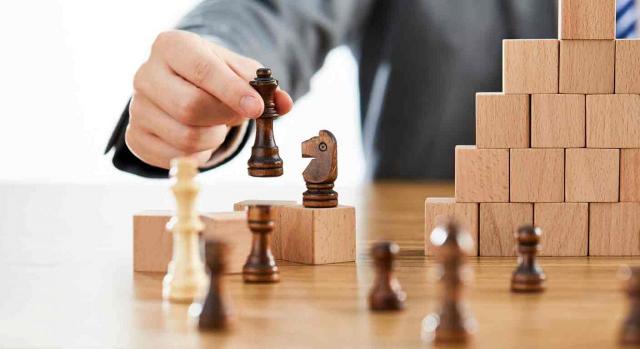 Un empresario, con varias piezas de ajedrez sobre la mesa, tiene una en la mano