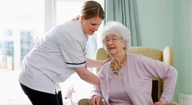 Accidente de trabajo. Servicio de ayuda a domicilio. Dolor lumbar que aparece de manera súbita tras levantamiento de usuaria. La prueba del accidente no requiere necesariamente testigos presenciales. Imagen de una enfermera ayudando a una señora mayor a levantarse de un asiento