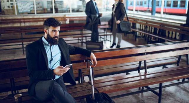 Desplazamiento; traslado; extinción indemnizada. Un hombre con el móvil en la mano sentado en una estación de tren prácticamente vacía