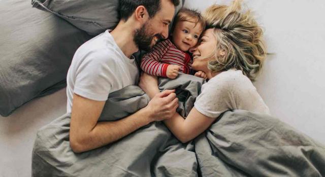 Una pareja con su bebé entre ellos sonríen en la cama