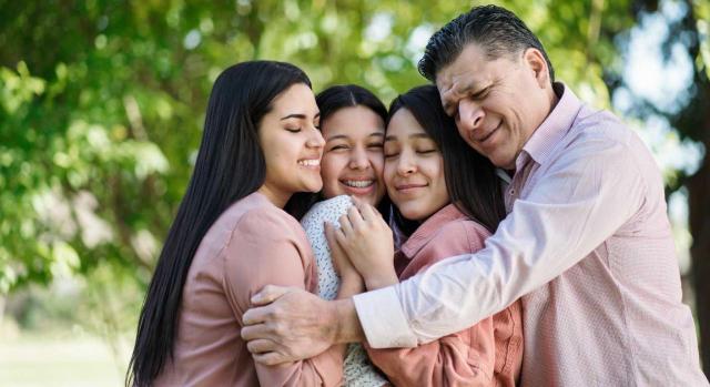 Tipos de arraigo y extranjeros con derecho a reagrupación familiar en España. Padre cariñoso abrazando a sus hijas en un jardín
