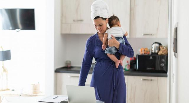 Familia monoparental. Mujer de pie con un bebé en brazos mientras usa el portátil