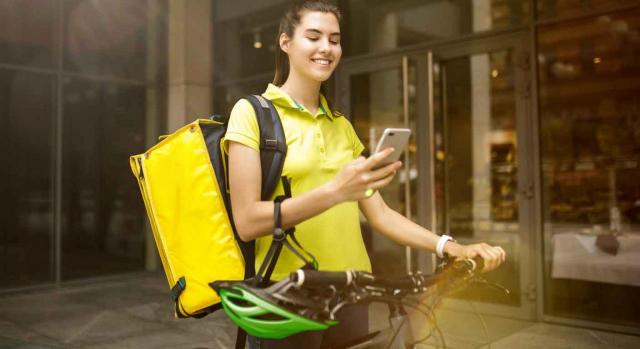 Imagen de una chica de la empresa glovo mirando su movil para ver donde tiene que llevar su reparto