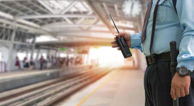 Convenios colectivos; jubilación parcial. Guardia seguridad sostiene un walkie-talkie en una estación de tren