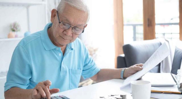 Jubilación; RETA; imputación de pagos. Hombre mayor en casa, usando calculadora, con unas monedas sobre la mesa y unas hojas en la mano