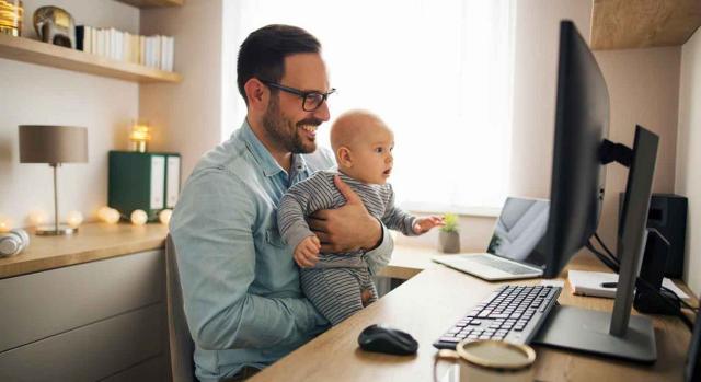 Control teletrabajo. Hombre con su hijo pequeño en brazos teletrabajando