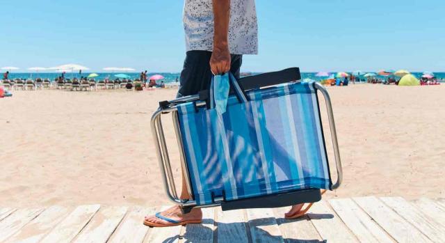 Vacaciones ERTE. Hombre entrando en la playa con una silla plegable