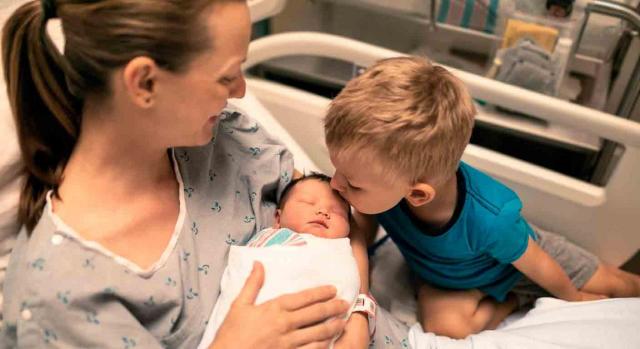 Hospitalización por parto. Mujer hospitalizada con bebe en brazos y acompañada de un niño