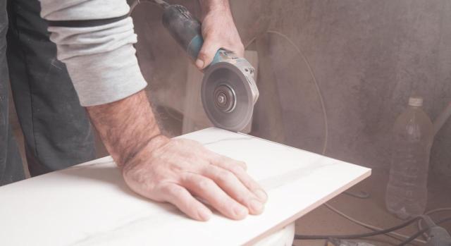 Debe reconocerse la prestación de IPT derivada de enfermedad profesional al trabajador (marmolista) diagnosticado de silicosis simple que se encuentra en situación de desempleo tras haber cesado en su última ocupación cotizada. Imagen de un trabajador cortando una baldosa con una amoladora