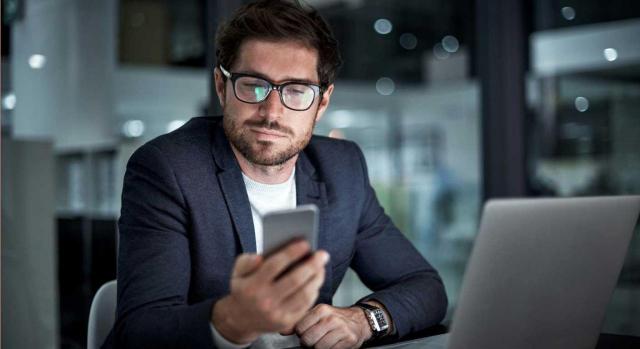 Jubilación parcial y contrato de relevo. Hombre sentado frente a una mesa con portátil, mirando la pantalla de un móvil