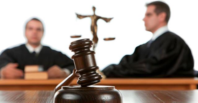 La viabilidad de la posterior acción de jactancia empresarial queda supeditada al criterio del juez del concurso Despido colectivo: la mera iniciación del periodo de consultas antes de la declaración de concurso no preserva la competencia de la jurisdicción social si la decisión extintiva se formaliza tras el auto concursal. Imagen de una maza en un escritorio y dos personas en el fondo difuminadas