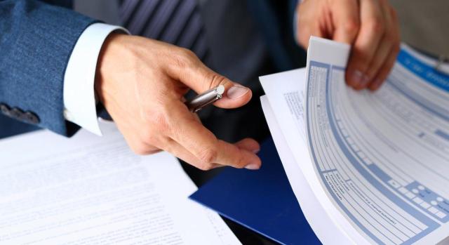 La concurrencia de seguros provoca una responsabilidad solidaria. Brazo de hombre con unos papeles sobre la mesa y un boli en la mano