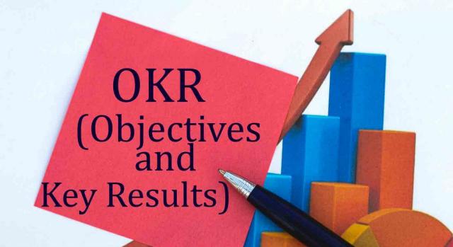 Metodologías CFR y OKR en el teletrabajo. OKR escrito en una hoja de papel rojo, con un bolígrafo encima sobre un fondo con gráficos