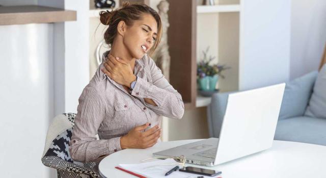 Baja laboral: quién puede emitirla y cuáles son las obligaciones de trabajadores y empresas. Imagen de una mujer sentada frente a su ordenador con gesto de dolor de cuello