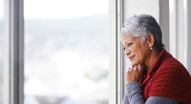 Viudedad; acrecimiento impropio. Mujer madura sonriendo, mirando a través de la ventana