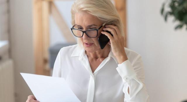 Jubilación forzosa o despido nulo/improcedente. Imagen de una mujer con cara de preocupación hablando por teléfono con un papel en la mano