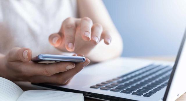 Incapacidad temporal. Extinción. Incomparecencia a reconocimiento médico habiendo efectuado citación la mutua por SMS Extinción de la IT por incomparecencia a reconocimiento médico. ¿Es válida la citación a través de SMS? Imagen de una mujer haciendo algo con su movil encima de un portátil