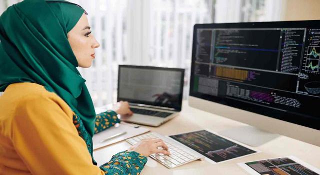 Discriminación; religión o convicciones. Mujer musulmana trabajando con un teclado y un ordenador a la vez