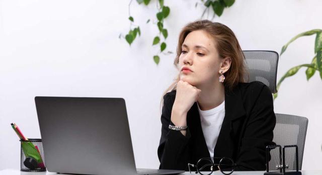 Desvinculación emocional en el trabajo: qué puede hacer RR. HH. para frenar esta tendencia Desvinculación emocional en el trabajo: qué puede hacer RR. HH. para frenar esta tendencia. Imagen de una chica sentada en la oficina con su portátil con cara de aburrimiento