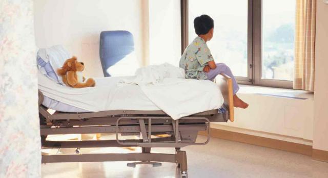 cuidado de hijo menor; cáncer u otra enfermedad grave; escolarización. Un niño sentado a los pies de la cama de un hospital y tiene un peluche en la almohada