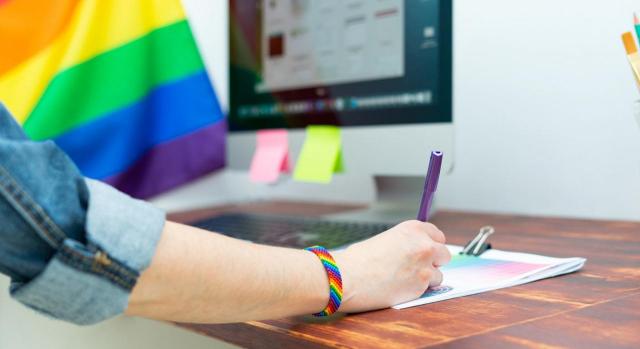 Causa sospechosa de discriminación. Imagen de mano de mujer trabajando en la oficina con decoración y accesorios LGBT