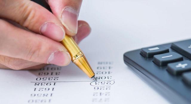 Actualización de importes vinculados al SMI 2024. Imagen de mano sosteniendo un bolígrafo y rodeando una cifra en un papel y una calculadora