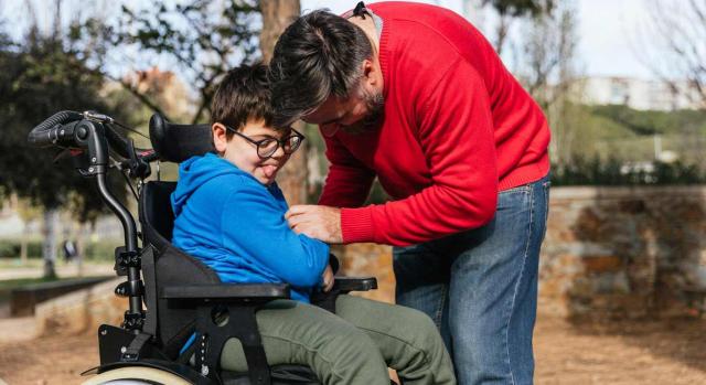 Ajustes razonables para trabajadores cuidadores. Padre jugando con su hijo con discapacidad en una silla de ruedas mientras disfrutan del tiempo juntos al aire libre en el parque