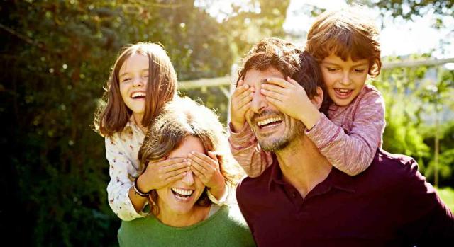 Complemento género. Dos niños subido a la espalda de su madre y su padre respectivamente y les tapan los ojos con las manos