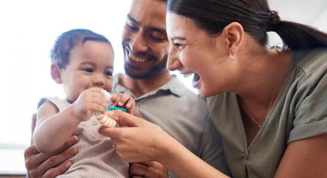 Prestación por maternidad; adopción; hijo biológico del cónyuge; gestación subrogada. Unos padres jóvenes y sonrientes con su bebé sentado en las piernas del padre mientras su madre juega con él