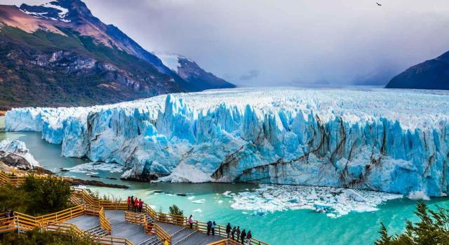 Jurisprudencia. Gente asomada a una barandilla observando un glaciar, las montañas y un río