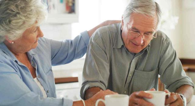 invalidez no contributiva; límite de acumulación de recursos; nietos; acogimiento familiar. Una pareja senior toman un café, ella tiene la mano en la espalda de el hombre mientras este mira su taza