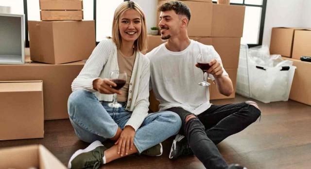 permisos retribuidos; matrimonio de parientes; traslado de domicilio habitual. Una pareja joven brindan sonrientes con una copa de vino rodeados de cajas por mudanza