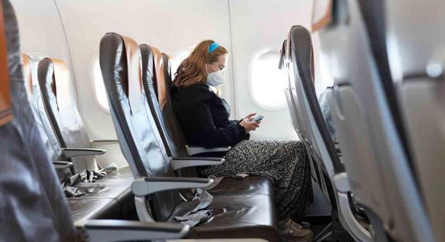 Una chica con mascarilla sentada en un avión vacio