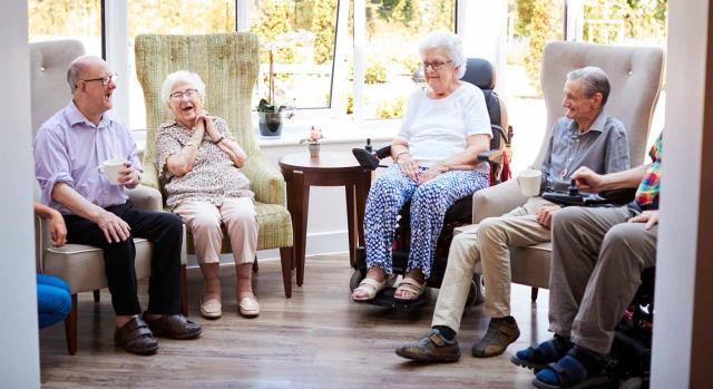 No existe una relación directa, frecuente o habitual. Residentes masculinos y femeninos sentados en sillas y hablando una residencia de mayores